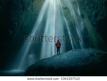 Iceland landscape photo of brave woman standing on slippery rock towards waterfall in mossy cave at spooky atmospere.