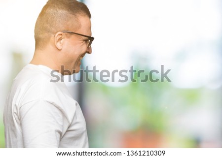 Middle age arab man wearig white t-shirt and sunglasses over isolated background looking to side, relax profile pose with natural face with confident smile.