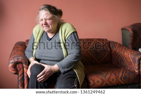 Old woman suffering from pain in knee. Elderly senior woman hasrheumatism pain in her legs. Unhappy woman in pain sitting on sofa at home, feel sick. Aged woman with knee pain. Rheumatoid disease.