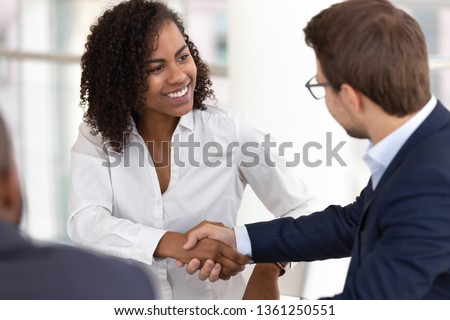 Smiling diverse businesswoman and businessman shake hands make partnership deal agreement at group office meeting negotiation thank for good teamwork expressing respect gender racial equality concept Royalty-Free Stock Photo #1361250551
