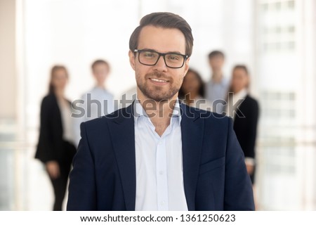 Confident business man coach in suit director company owner professional manager looking at camera with team on background, smiling male ceo leader banker employer posing in office, headshot portrait Royalty-Free Stock Photo #1361250623