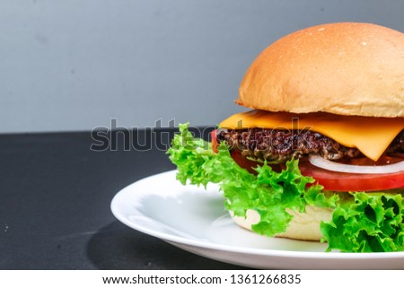 Close-up homemade fresh and juicy burger with beef patty, cheese, lettuce, onion, tomato on the white plate, dark table and space for text. - Image
