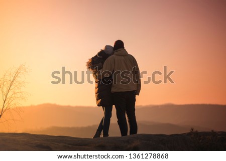 Silhouettes of a man and woman on mountain peak at sunrise.