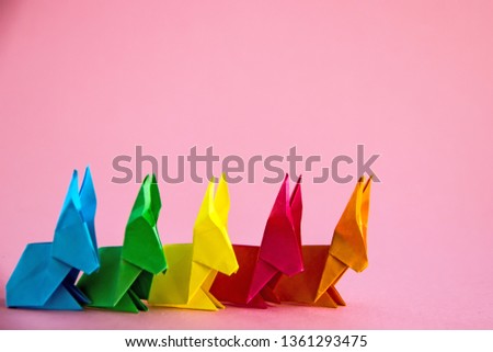 Paper multicolored origami rabbits on a pink background, copy space. Easter concept, creativity concept.  