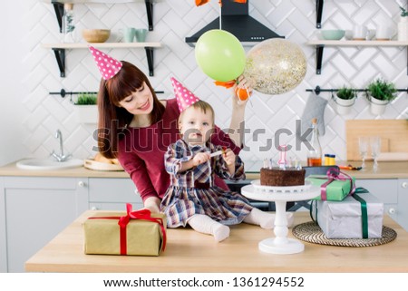 Portrait of happy mother and daughter on her first birthday party, indoors