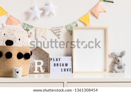 Stylish and modern scandinavian newborn baby interior with mock up photo or poster frame on the white shelf. Toys, teddy bear, plush rabbit and hanging cotton colorful flags and star. Template. Blank.