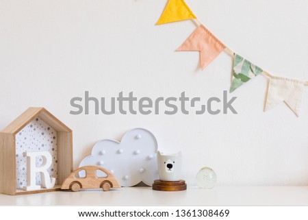 Stylish and modern scandinavian child room with hanging cotton colorful flags on the white wall, box, teddy bear's cup, toys. wooden accessories and cloud. Real photo. Copy space. Cozy decor.