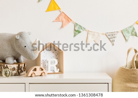 The modern scandinavian newborn baby room with plush rhino, design toys and box on the white shelf. Hanging cotton flags on the white background wall. Stylish and cozy interior. Copy space. Real photo