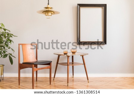 Stylish and design retro interior with design chair, gold lamp, small table with accessories. Black mock up frame on the grey background wall. Minimalistic concept of sitting room. Real photo. 