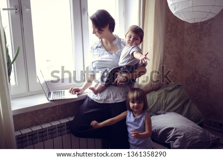 Mom with children working on a laptop near the window, the children are waiting for a cartoon