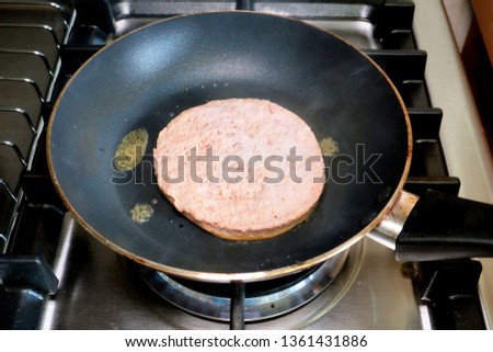 A picture of a raw homemade lamb patty been cooked in the frying pan. 