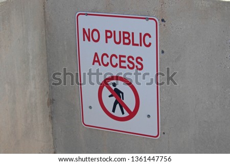 No Public Access Sign in black capital letters includes silhouette of person and red prohibition sign with white background; hanging on concrete wall