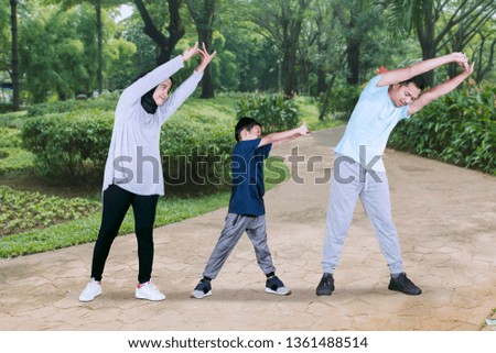 Picture of a little boy doing hands stretch while exercising with his parents in the park