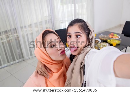 Two sisters taking selfie photos together with happy expression before breaking the fast in the kitchen