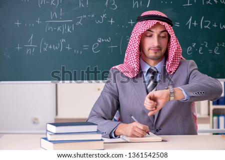 Arab teacher wearing suit in front of chalkboard  
