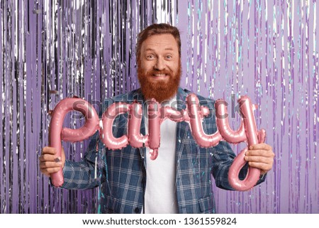 Millennial cheerful guy with red hair, ginger thick beard, comes on stag party to best friend, wears elegant checkered jacket, poses with letter shaped balloons over bright purple background