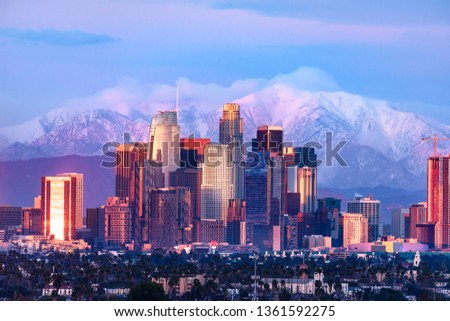 Downtown Los Angeles skyline with snow capped mountains behind at sunset
