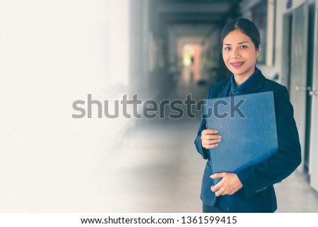 A beautiful young Asian business secretary is standing smiling confidently. Before bringing documents to the meeting about the business to sign for approval.