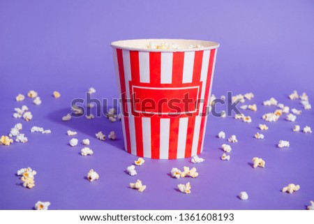 Close up photo of tasty salted sugary different mixed tastes popcorn in striped paper cup little small pieces thrown everywhere isolated on purple violet bright background