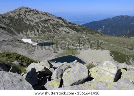 A beautiful view high up in the mountain. You can see a lake, stones, grass, peaks, ridge and white clouds on the blue sky. The photo is taken on a summer July day, in mount Pirin, Bansko, Bulgaria.