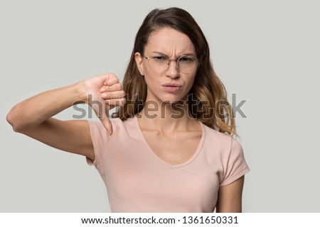Dissatisfied young attractive woman wearing eyeglasses looking at camera showing thumbs down gesture symbol of negative feedback, bad quality evaluation and dislike, disagreement and rejection concept Royalty-Free Stock Photo #1361650331