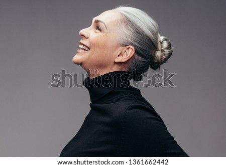 Side view of senior woman laughing on gray background. Profile view of mature woman in black casuals looking happy Royalty-Free Stock Photo #1361662442
