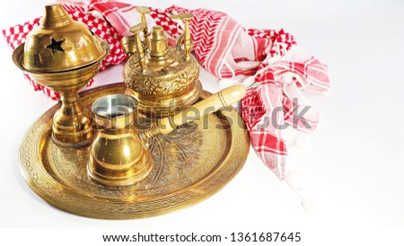 Arabic coffee set on brass tray with traditional Arab style scarf on white background.
