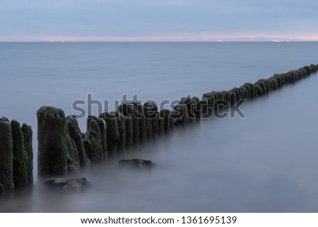 Long exposure photo of a wooden wavebreaker in the evening. Port or ship lights visible in the background.