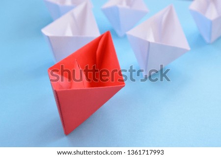 A red self-folded paper boat lies on a blue surface, followed by many white boats - concept symbolizing leadership 