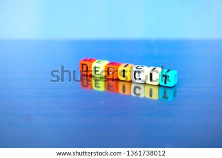Conceptual image of deficit cash flow position. Alphabet beads spelt deficit over blue background. Focus on beads closer to foreground.