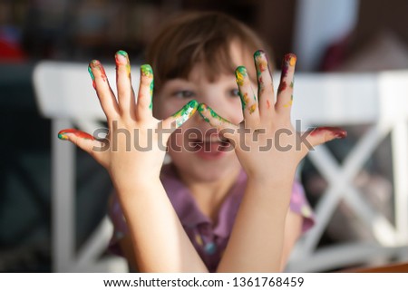 Cute little preschool gir having fun, looking at her painted hands and smiling. Education, school, art and painitng concept