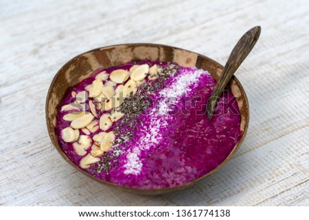 Red smoothie in coconut bowl with dragon fruit, avocado, almond flakes, coconut chips and chia seeds for breakfast , close up. The concept of healthy eating, superfood . Island Bali, Indonesia