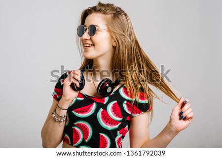 Young caucasian woman in sunglasses with headphones posing on grey background