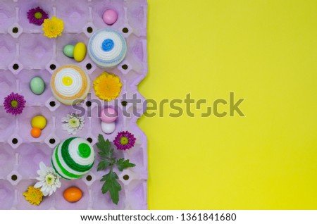 Colorful eggs decorate with knitting wool for Easter day and festival put in purple egg tray with colorful Chocolate and chrysanthemum flowers on yellow background that have space for text.