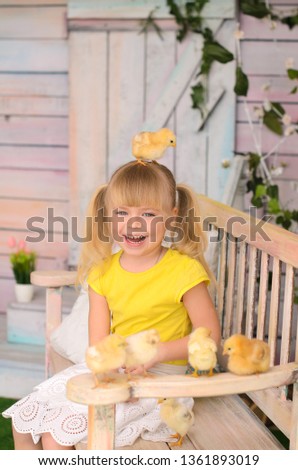 Little girl blonde in yellow T-shirt, sitting on bench, playing with chickens