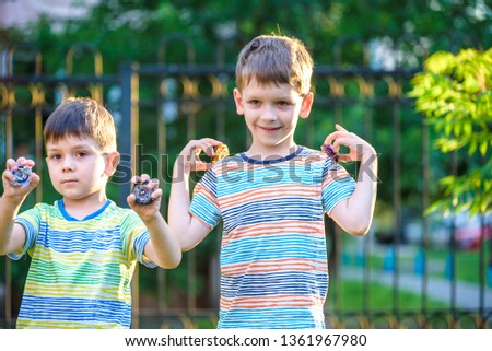 Two brother boy playing with modern spin top outdoors. Entertainment game for children. Top, triggered by a trigger. Kids demonstrate two different variants choosing which is better.