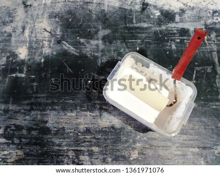 White paint can and roller brush on a dark grunge table with scratches, copy space