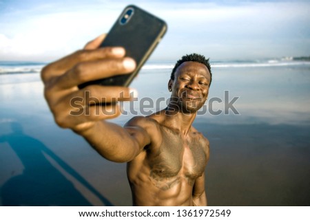 young attractive and happy black afro American sport man with athletic body and sixpack taking selfie photo with mobile phone at beautiful beach smiling cool in holidays and travel concept