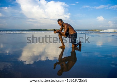 young attractive and happy black afro American sport man with athletic body  taking selfie photo with mobile phone at beautiful beach smiling cool in holidays and travel concept