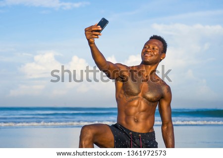 young attractive and happy black African American sport man with athletic body and sixpack taking selfie photo with mobile phone at beautiful beach smiling cool in holidays and travel concept
