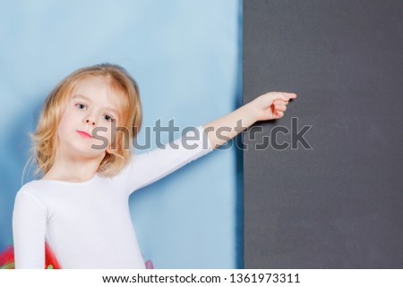 The little girl with a fair hair shows a finger on empty space on a black background. Beautiful cute baby. Bright advertising photography.