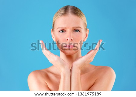 Close up portrait of gorgeous beautiful and good-looking young woman with flawless skin. She is palming her cheek isolated on blue background