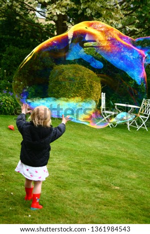 little girl in red wellies chasing giant bubbles in the garden