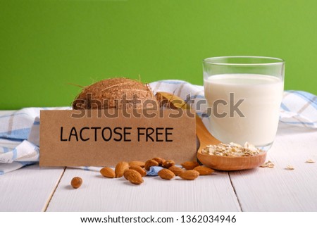 Lactose free milk. Glass of milk, almond nuts, oat flakes, coconut and piece of paper with text LACTOSE FREE on wooden surface on green background. Lactose intolerance food concept