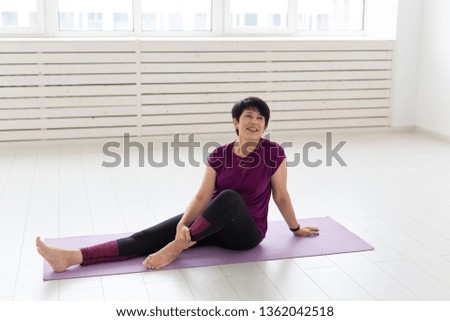 People, sport, yoga and healthcare concept - Smiling middle-aged woman sitting on exercise mat