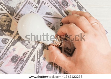 male hand with a light bulb on the background of money