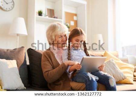 Portrait of grandmother reading stories to cute little girl using digital tablet together, copy space