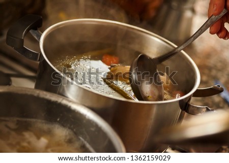 Hot stock pot is stirred by a ladle while it is simmering