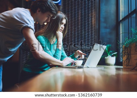 Caucasian male and female freelancers cooperating togetherness on laptop computer editing data inside application settings, millennial skilled hipsters searching information on content websites