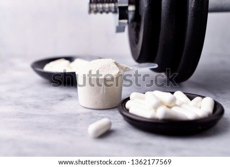 Scoop of Whey Protein, Creatine, Taurine capsules and a dumbbell. Bodybuilding food supplements on stone / wooden background. Close up. Copy space. Royalty-Free Stock Photo #1362177569